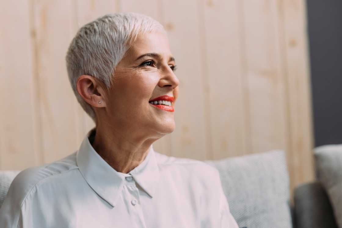 A senior woman with a short crop haircut poses while sitting. A senior woman with a short crop haircut poses while sitting.