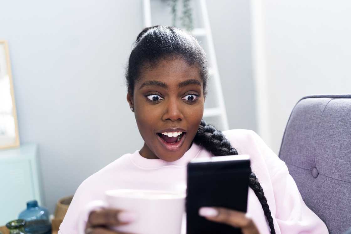 Surprised woman using mobile phone while sitting on sofa at home