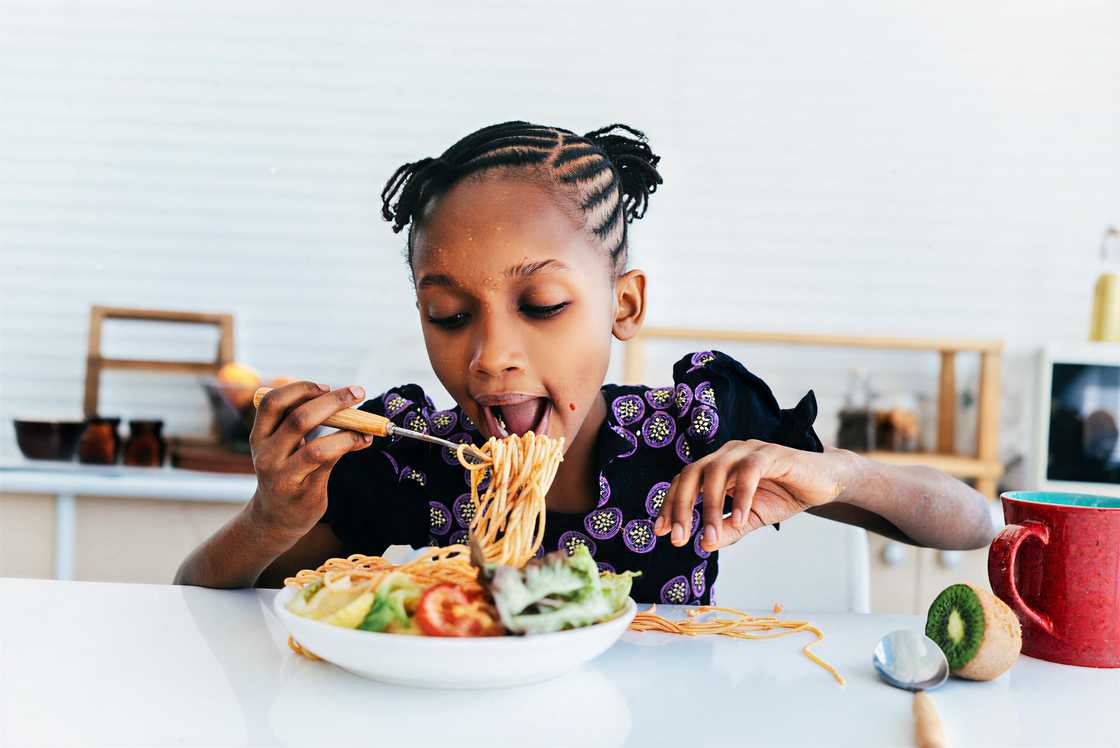 An African girl enjoys eating spaghetti An African girl enjoys eating spaghetti