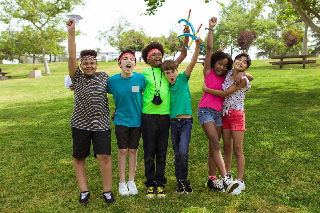 A group of kids raising their hands hhile standing on the grass