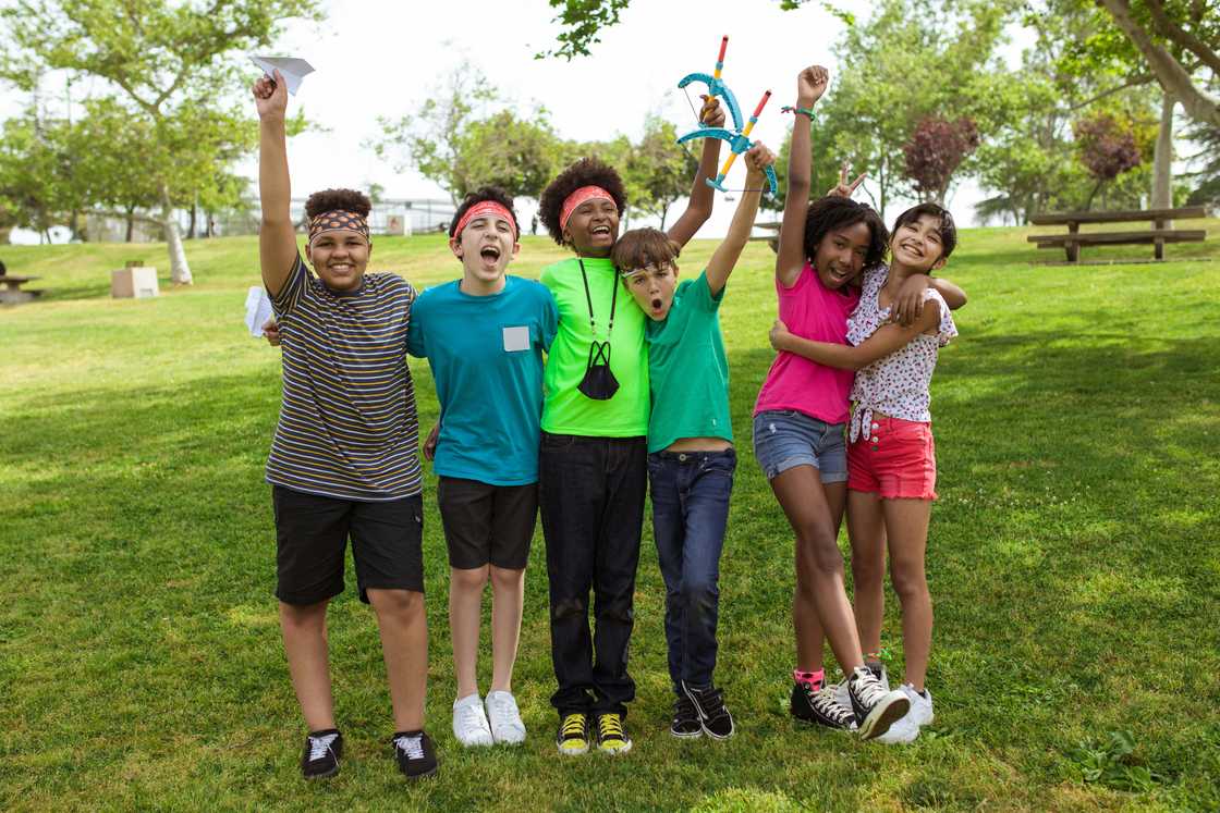 A group of kids raising their hands hhile standing on the grass A group of kids raising their hands hhile standing on the grass