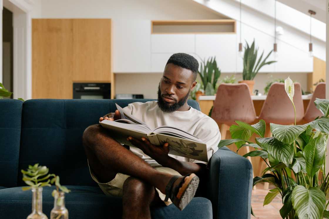 A young man is reading a book on a blue couch