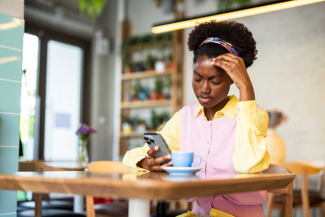 A stressed woman while using a smartphone in a coffee shop