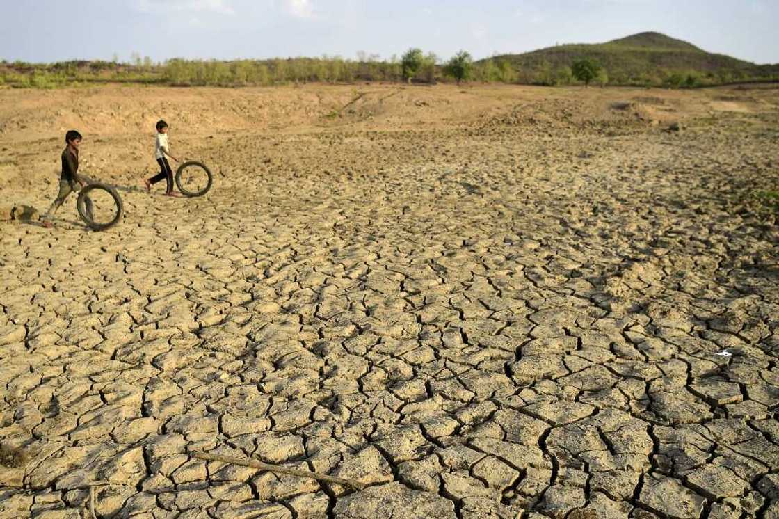 Children play with discarded cycle tyres as they walk on a dried up pond in Agrotha