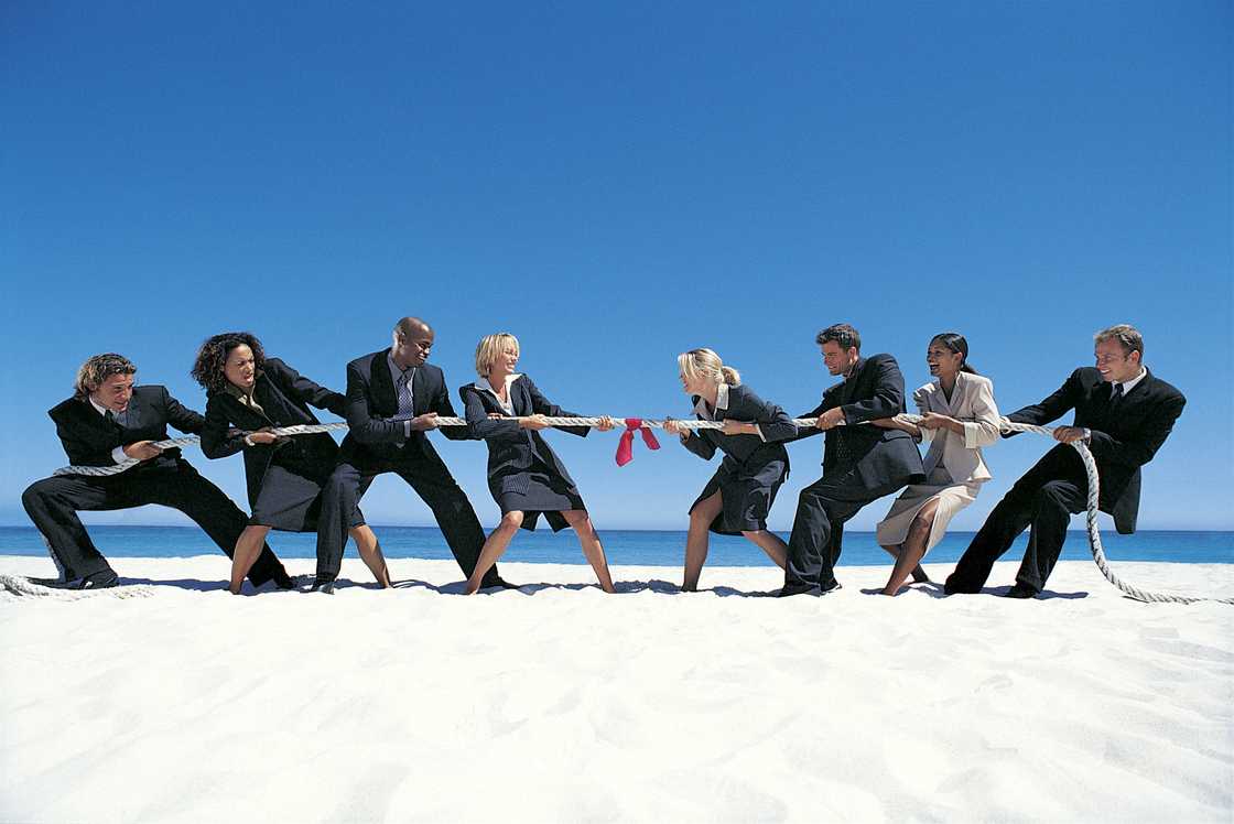 Business people playing Tug-of-War on the beach.