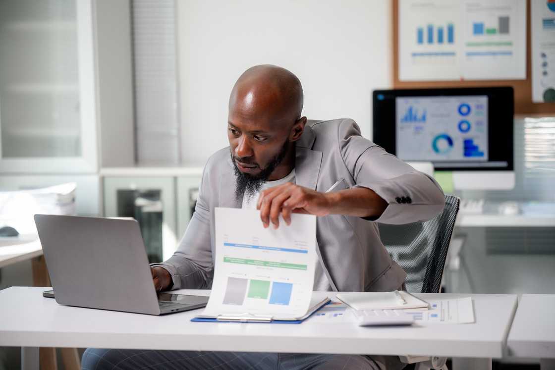 A man analysing financial data on his laptop and paperwork