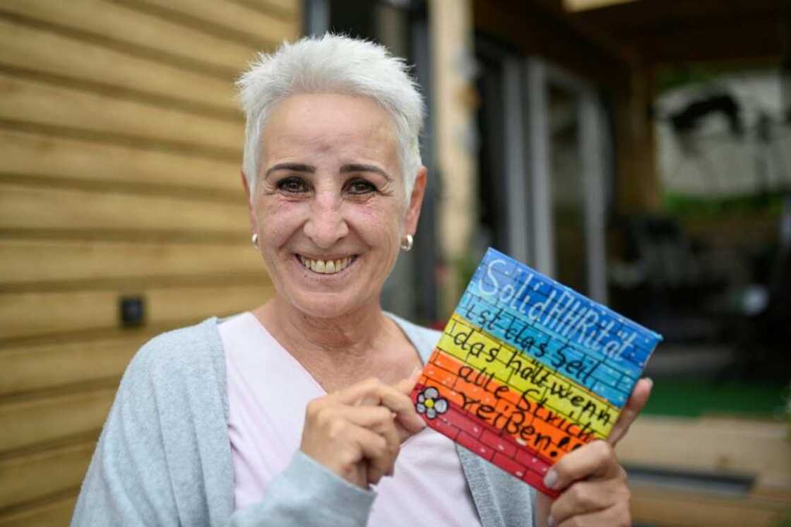 Anke Barteit at her tiny home in Bad Neuenahr, holding a sign that reads 'Solidarity is the rope that holds when everything else fails'