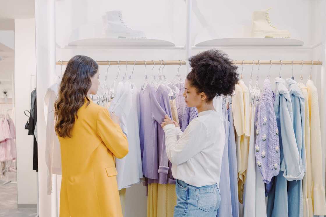 Two women browsing pastel clothing on racks inside a boutique.