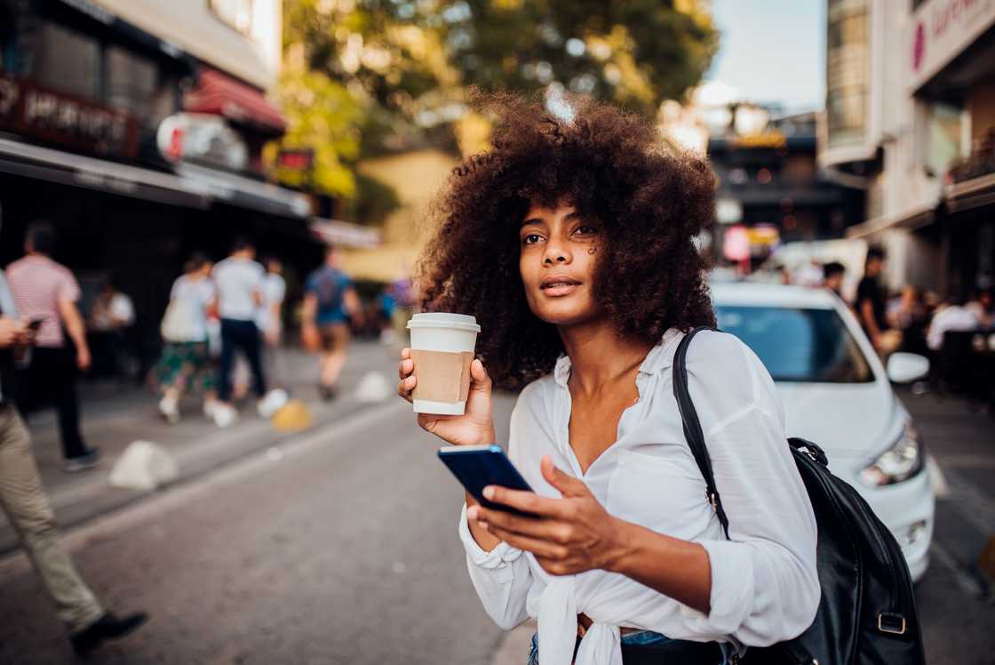 A lady holding a cup of coffee and phone in the streets