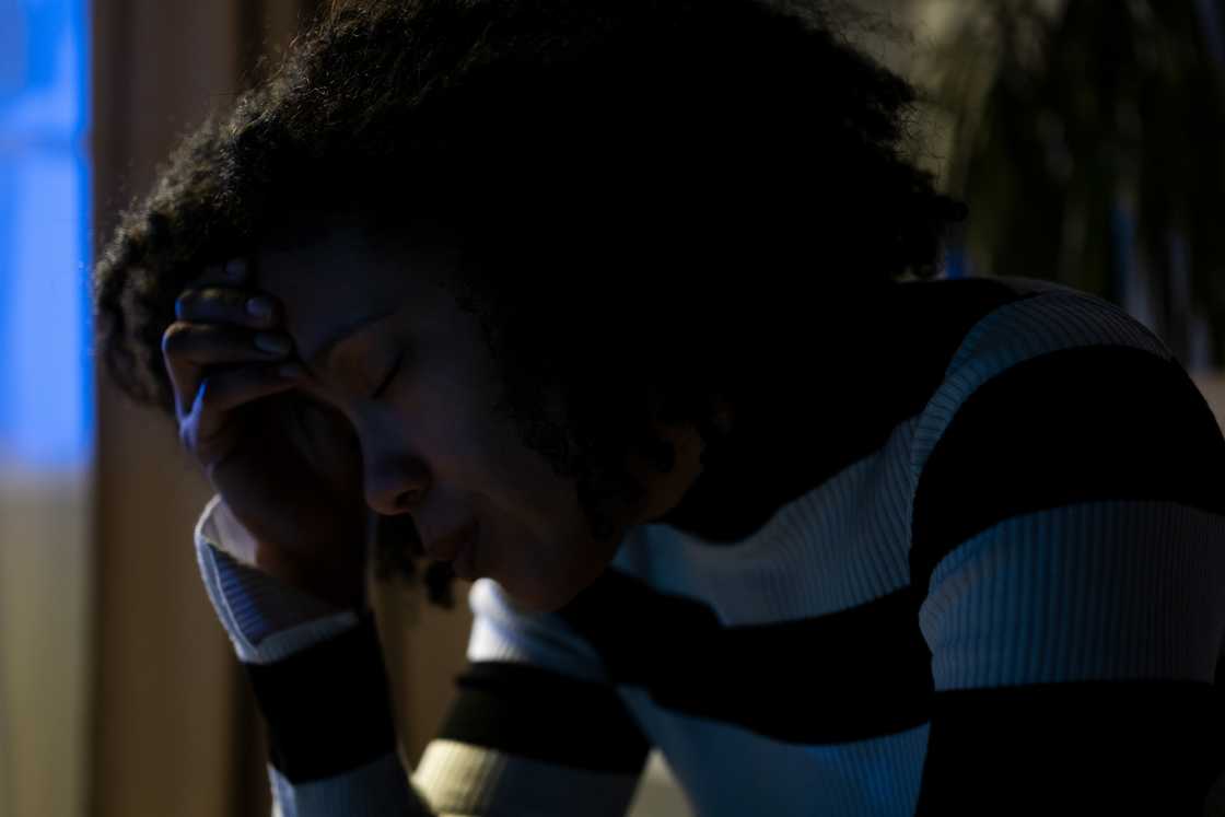 Person in striped shirt rests head on hand in a dimly lit room.