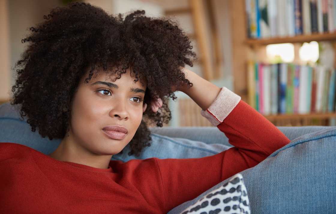 A young woman lost in thought and smiling while sitting on a sofa A young woman lost in thought and smiling while sitting on a sofa