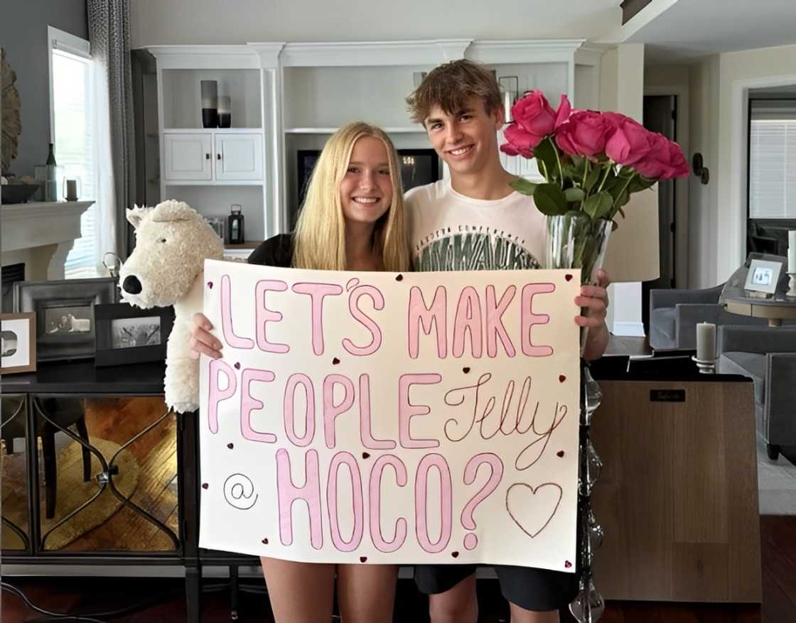 A couple holding a Homecoming proposal poster with a stuff dog and flowers