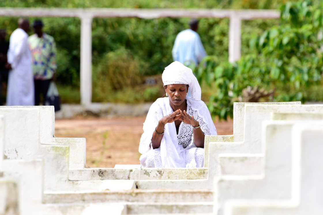 A woman stands by a grave, mourning.