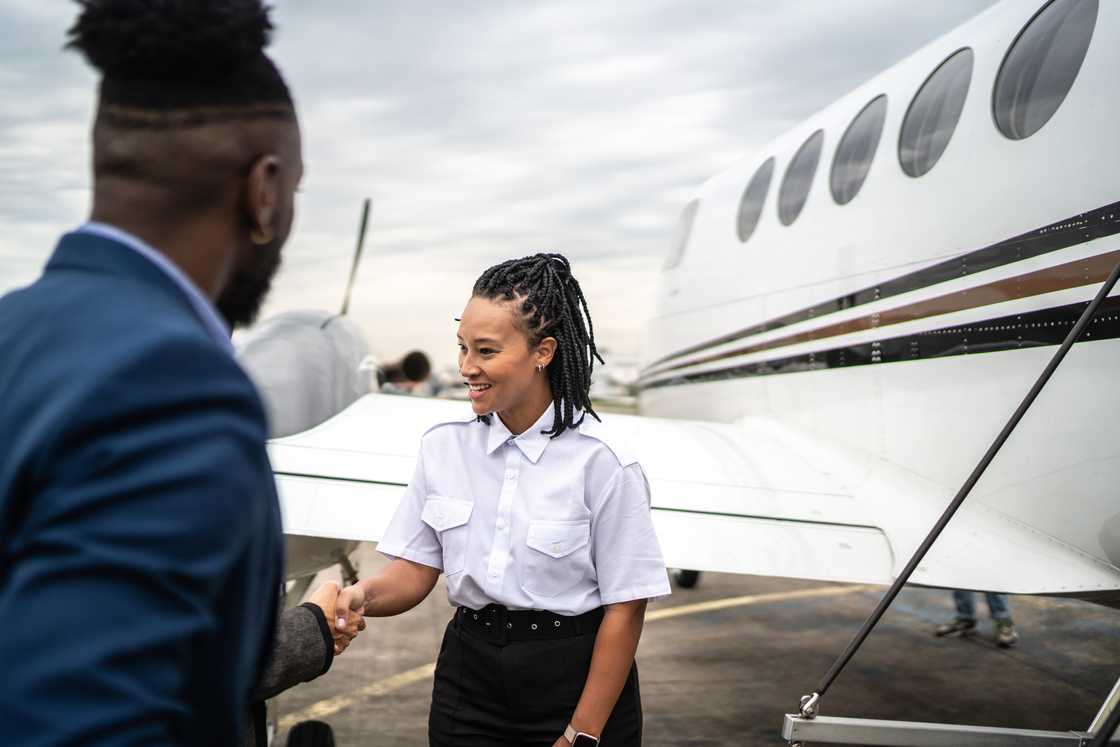 A woman in a white pilot's shirt shakes hands with a man in a navy suit near the jet's boarding stairs.