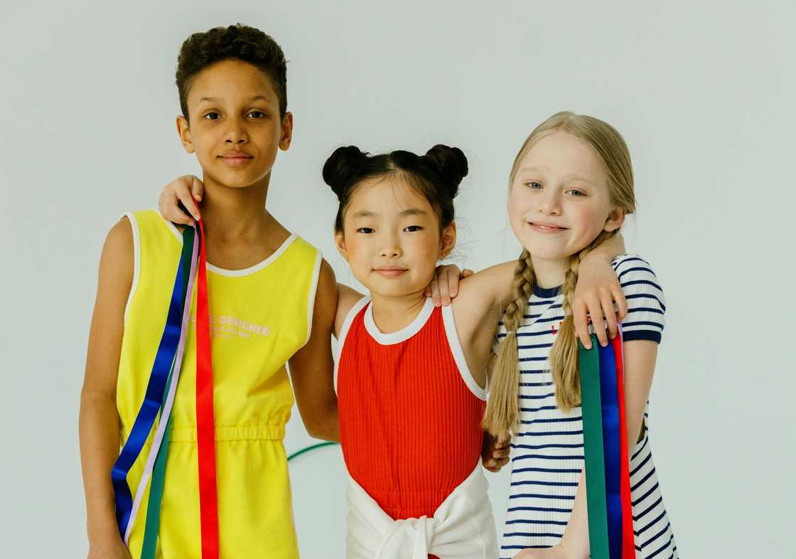 Three children stand together smiling with colourful ribbons.