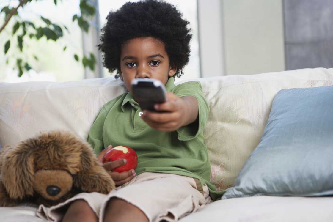 A kid holds a tv remote and an apple A kid holds a tv remote and an apple