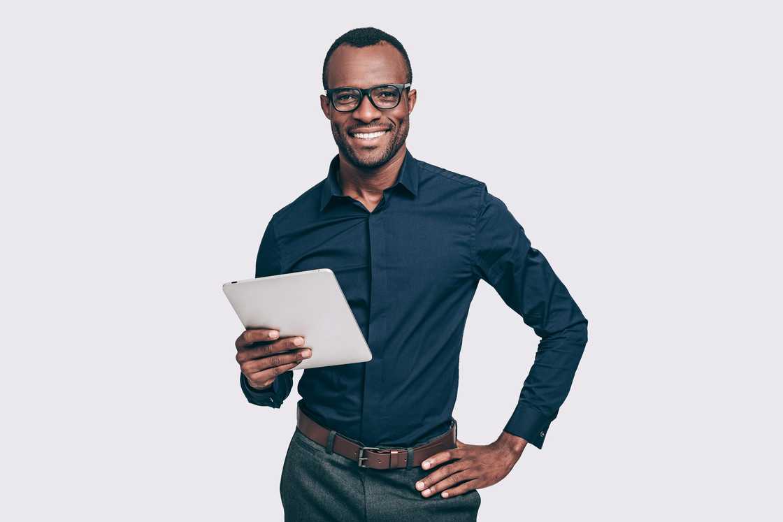 Man waering a dark blue button-down shirt, holding digital tablet and looking at the camera.