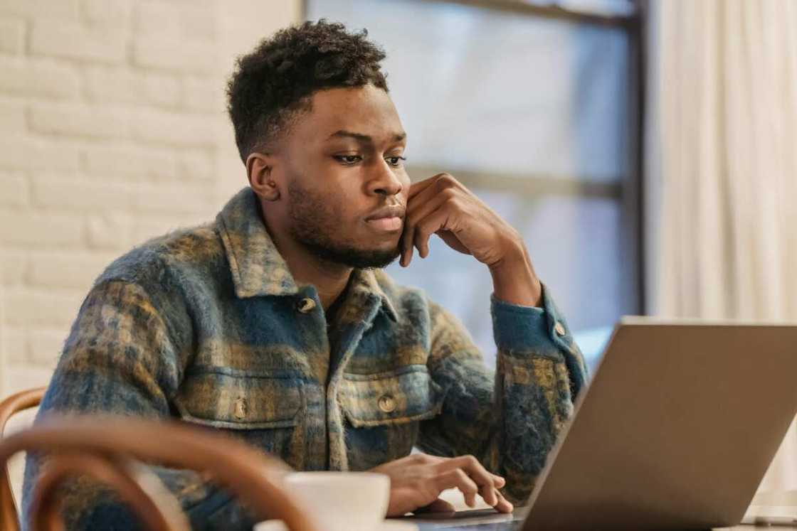 A serious man in a checkered jacket is using a laptop