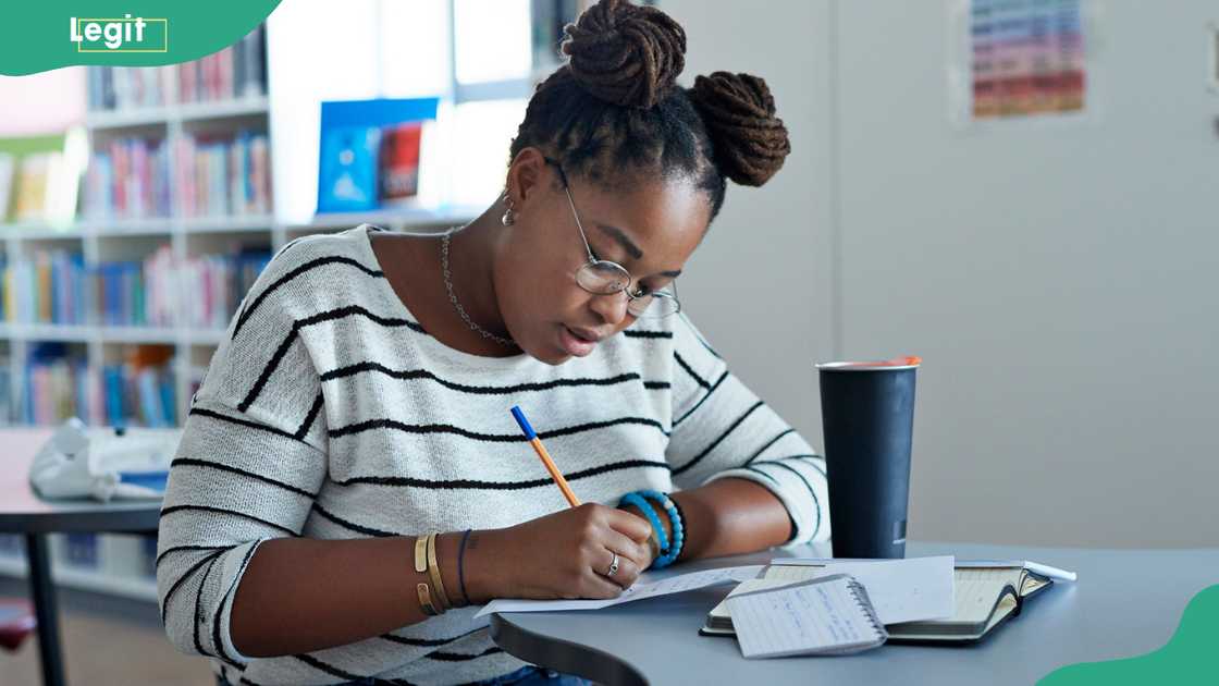 A female university student writes on paper while sitting at a desk in the library.