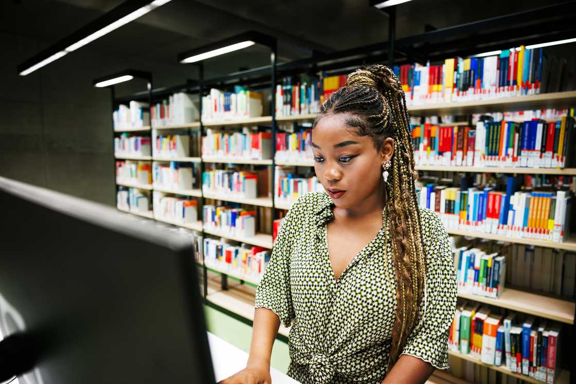 A young woman attentively working on a computer in a library filled with colorful books A young woman attentively working on a computer in a library filled with colorful books