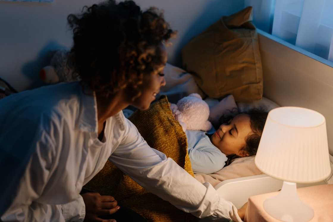 Mother switching off a bedside lamp while her child sleeps. Mother switching off a bedside lamp while her child sleeps.