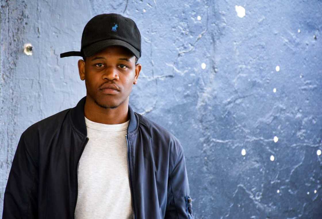 A man in a cap stands in front of a blue background