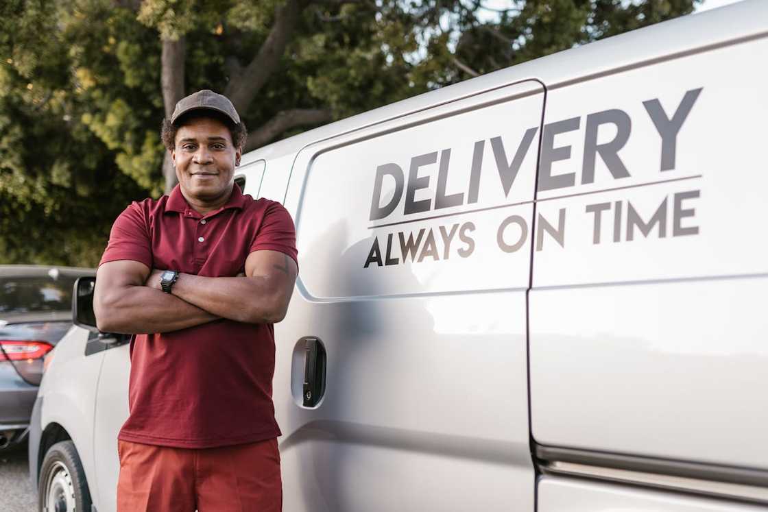 A delivery worker stands confidently beside a van with delivery signage.