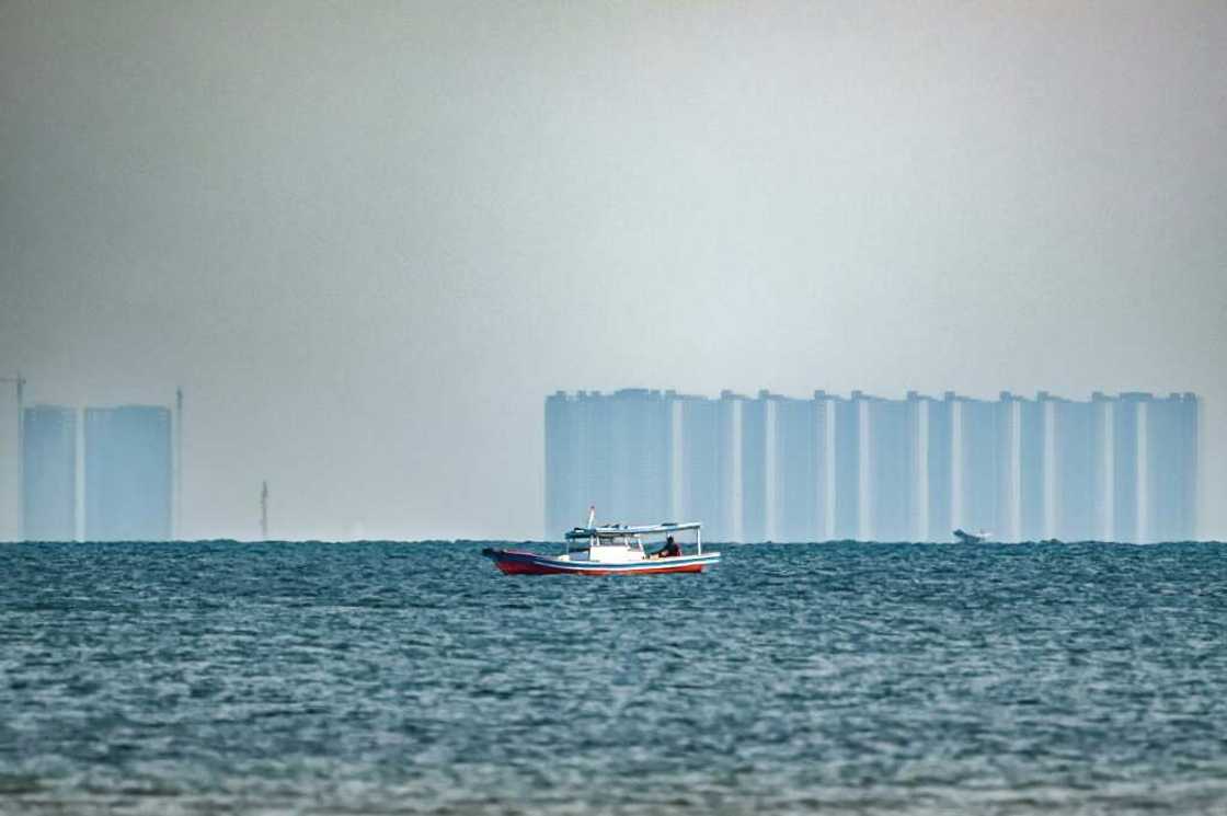 A man fishes off Pari, as buildings located in the northern part of nearby Jakarta are seen in the distance