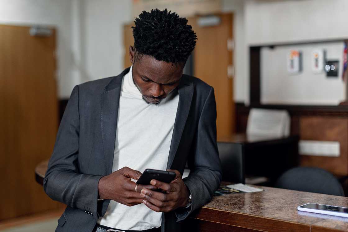 A man in a grey jacket and white tee using a smartphone