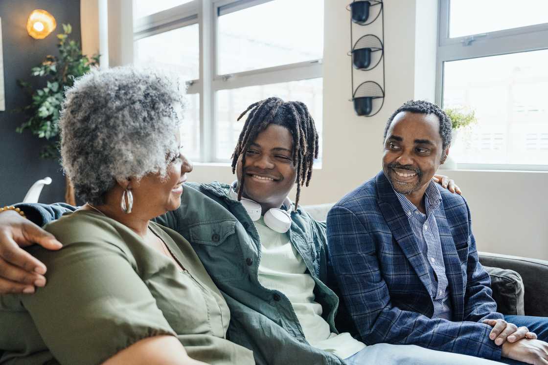 Three people sit closely together on a couch in a well-lit room. Three people sit closely together on a couch in a well-lit room.