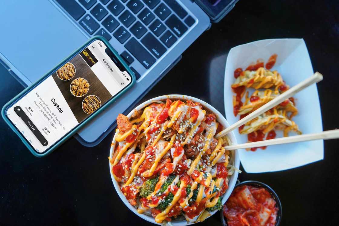 A phone with a confirmation for an order from Cupbop. A cup of Korean BBQ with sides A phone with a confirmation for an order from Cupbop. A cup of Korean BBQ with sides