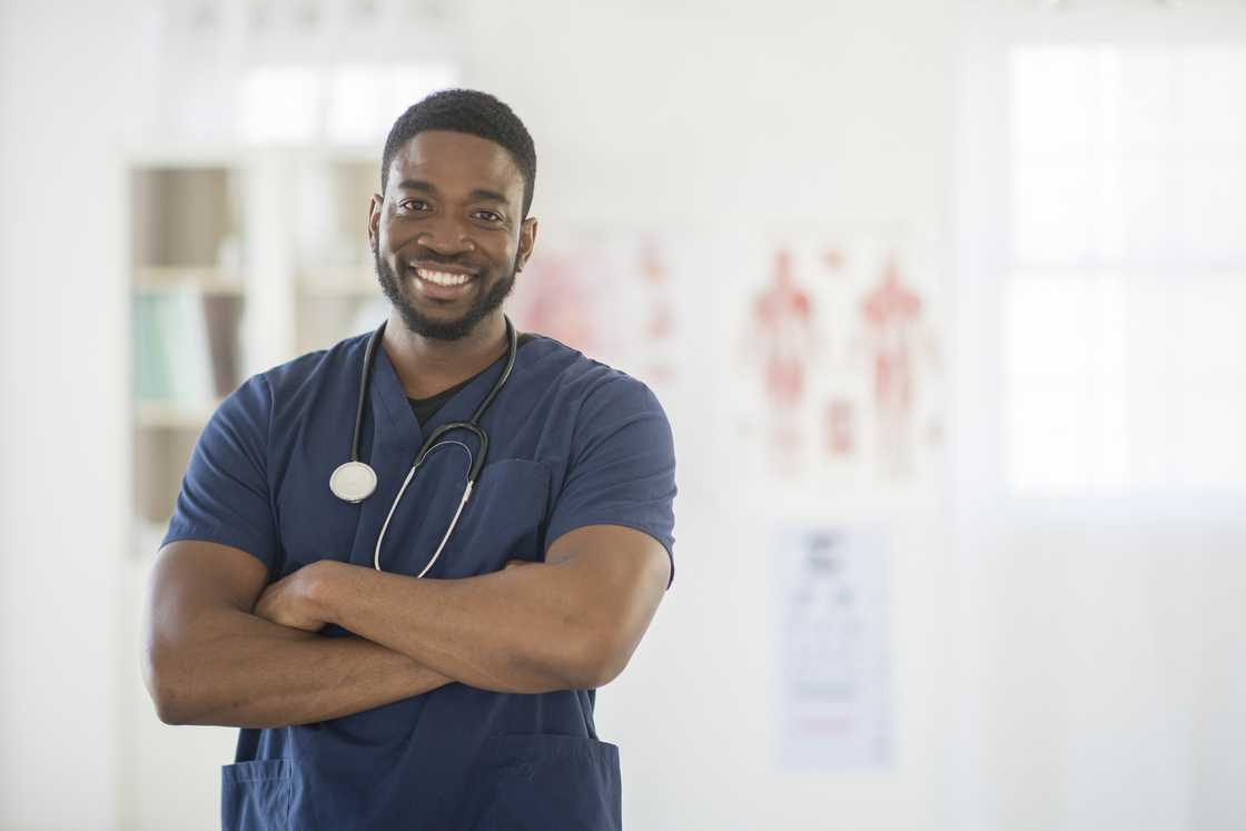A male nurse is standing in the doctor's office wearing scrubs and a stethoscope