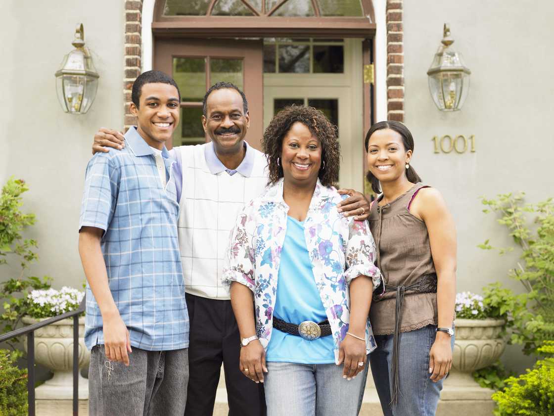 Four people stand smiling in front of a house.
