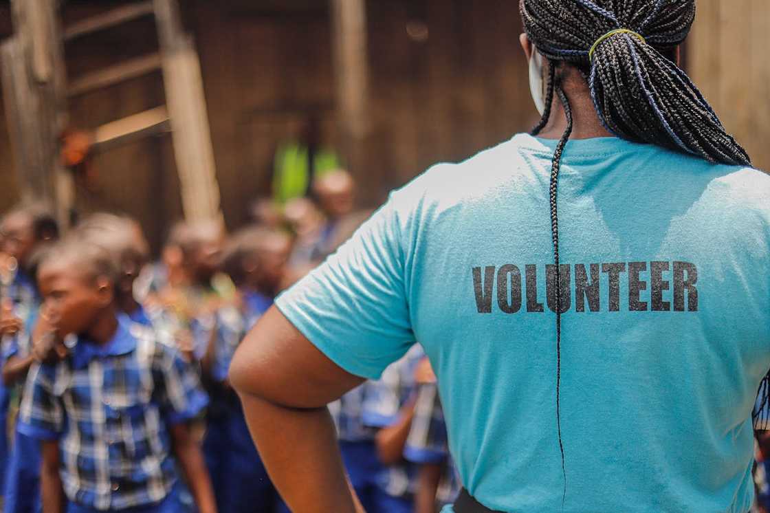 A volunteer stands facing a group of schoolchildren. A volunteer stands facing a group of schoolchildren.