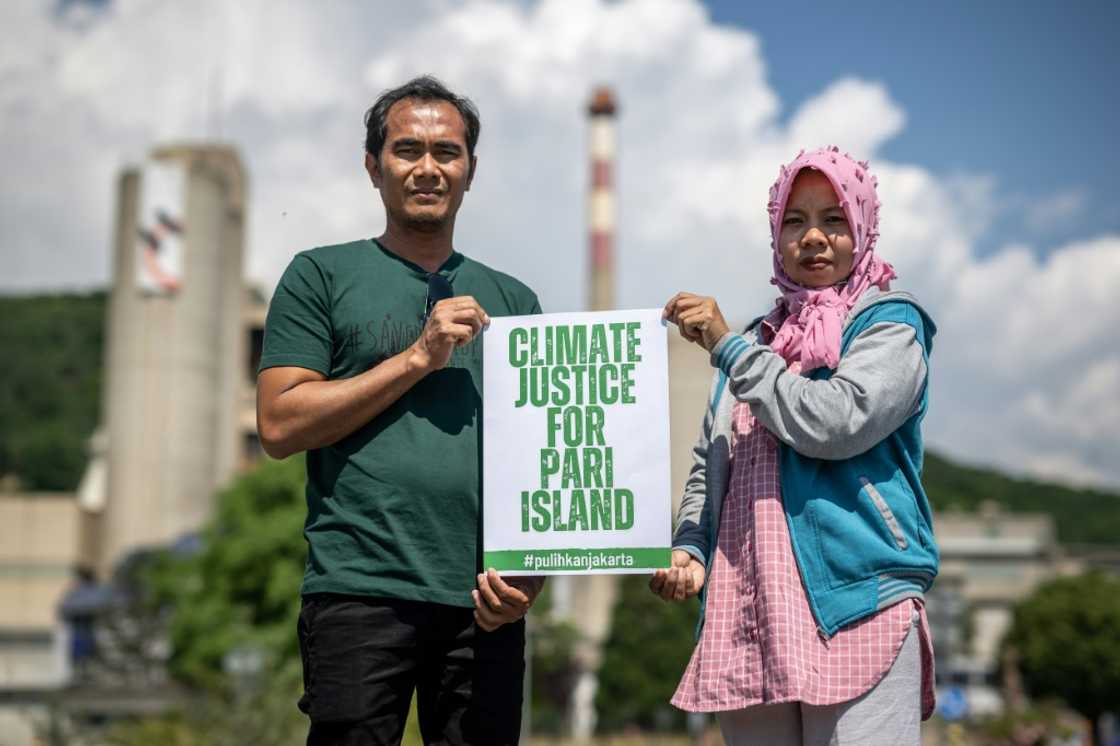 Pari island residents Edi (L) and Asmania pose next to the factory of Swiss cement giant Holcim in Eclepens, western Switzerland Pari island residents Edi (L) and Asmania pose next to the factory of Swiss cement giant Holcim in Eclepens, western Switzerland
