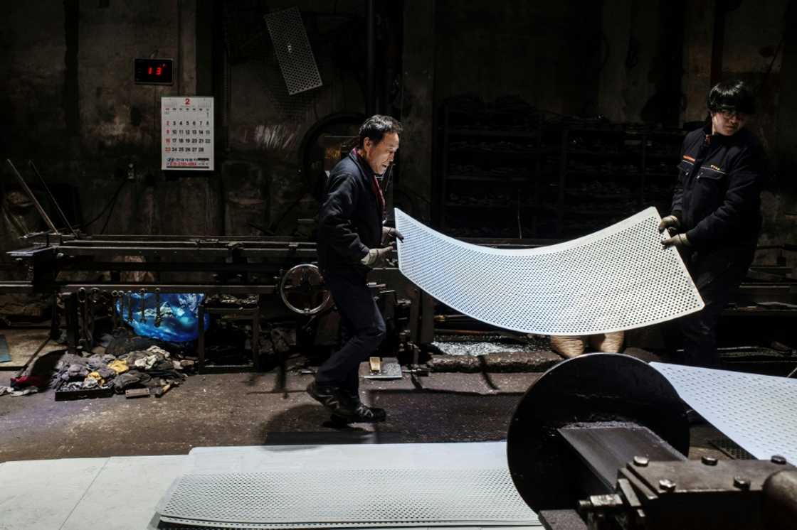 Employees carry a steel sheet after passing it through a perforating machine at a metal fabrication plant in Seoul