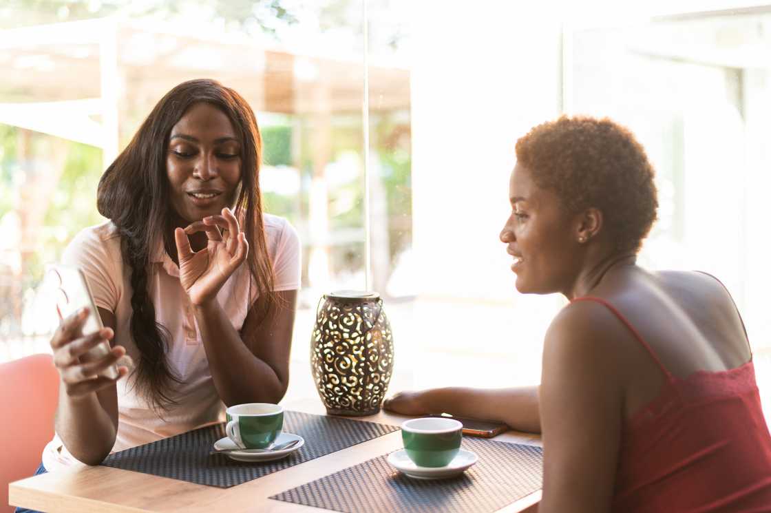 Two people sit at a table with drinks, looking at a phone together. Two people sit at a table with drinks, looking at a phone together.