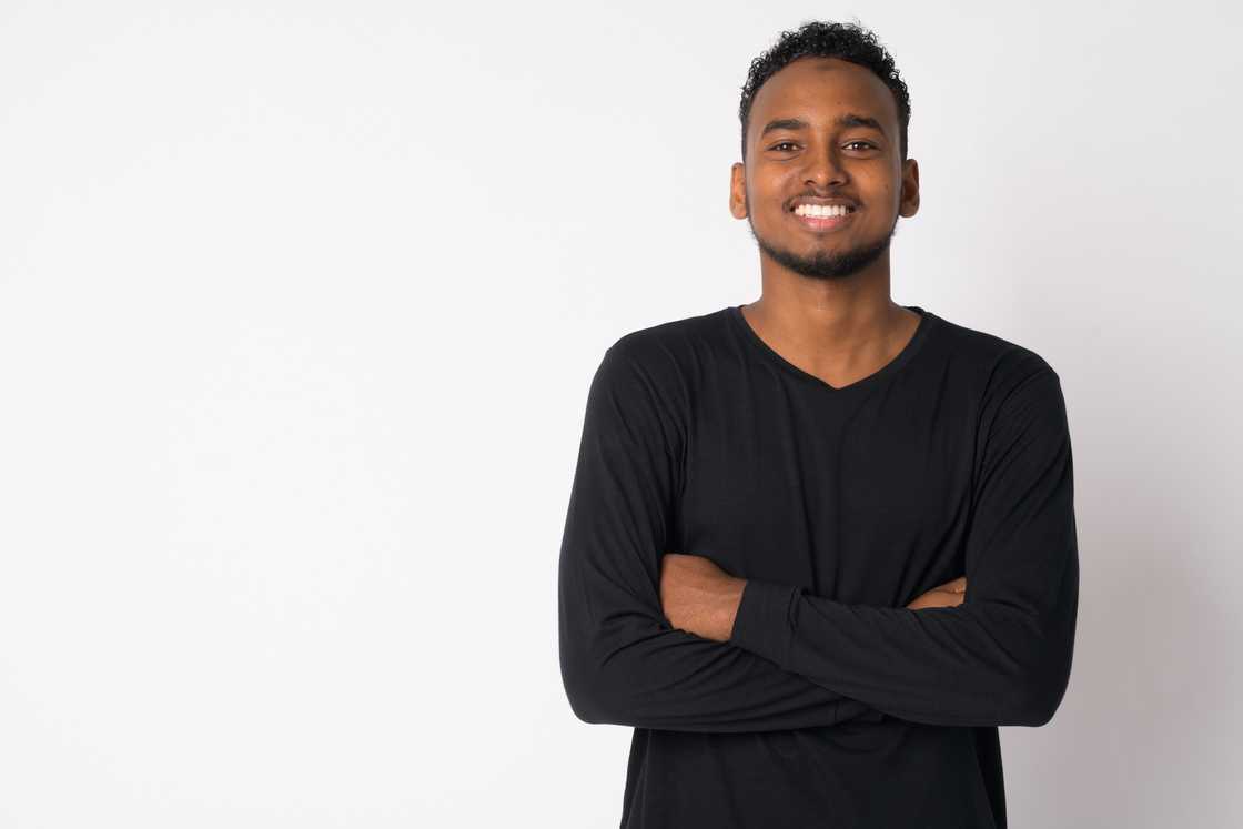 A young man wearing a long-sleeved shirt standing against white background.