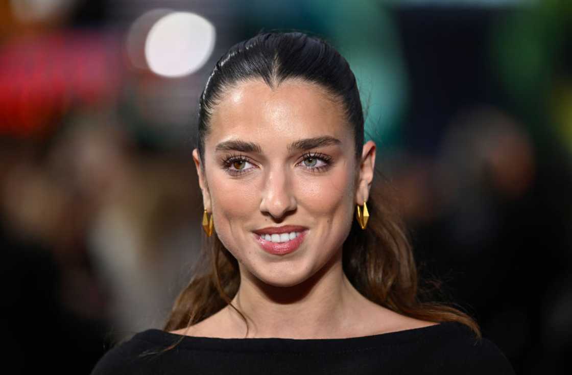 Close-up of a woman with slicked-back dark hair and gold geometric earrings.