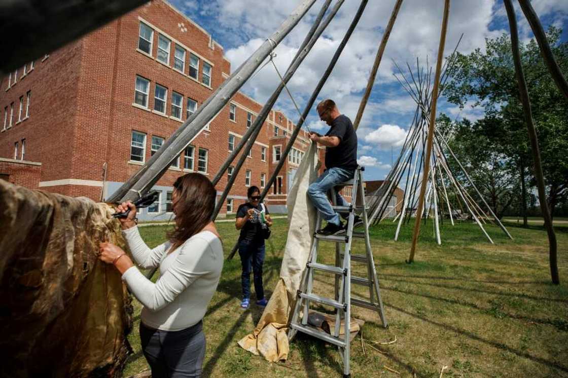 Jay Williams (C), of Saddle Lake First Nation, climbs atop a ladder as he and Joi Arcand attach a moose hide to a teepee outside the University nuhelt'ine tahiyots'i nistameyimakanak Blue Quills in St Paul, Alberta, Canada Jay Williams (C), of Saddle Lake First Nation, climbs atop a ladder as he and Joi Arcand attach a moose hide to a teepee outside the University nuhelt'ine tahiyots'i nistameyimakanak Blue Quills in St Paul, Alberta, Canada
