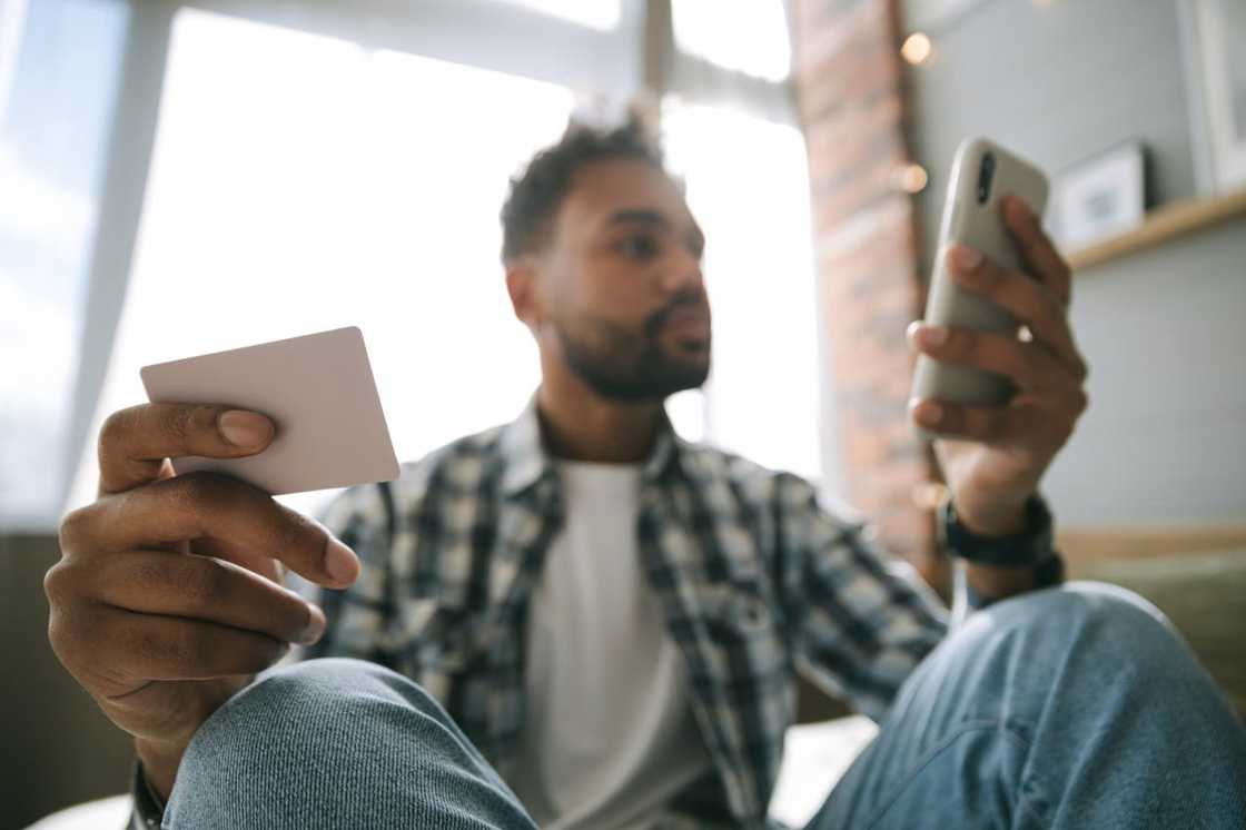 A man holds a card while looking at his phone.