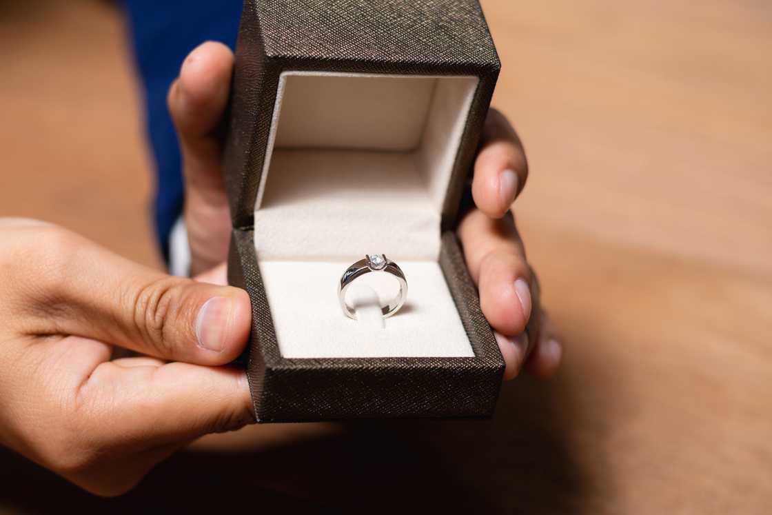 A man's hands holding a ring box with a wedding ring.
