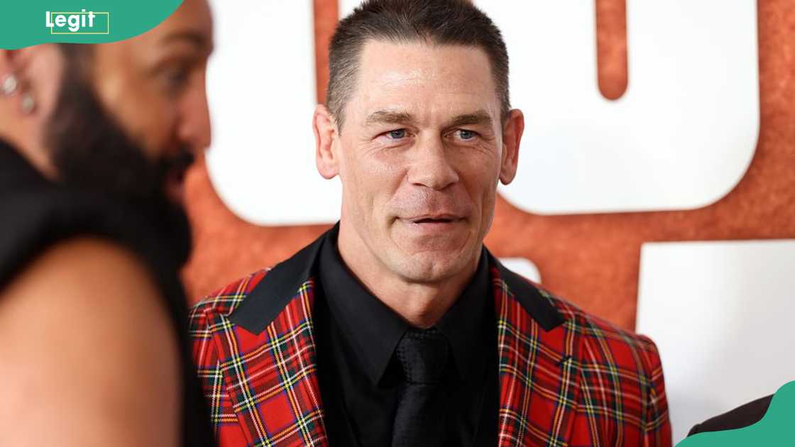John Cena smiling at the camera in a red tartan blazer and black shirt at the Los Angeles premiere of Coyote vs. Acme in Westwood, 2026 John Cena smiling at the camera in a red tartan blazer and black shirt at the Los Angeles premiere of Coyote vs. Acme in Westwood, 2026
