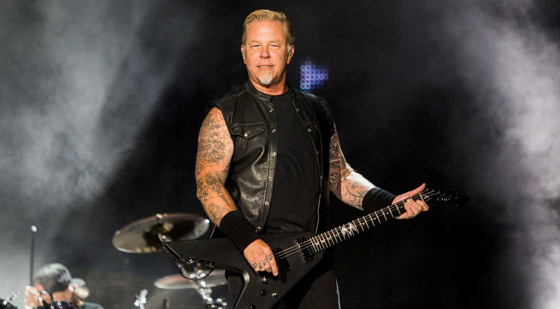 James Hetfield performs while holding and playing a guitar.