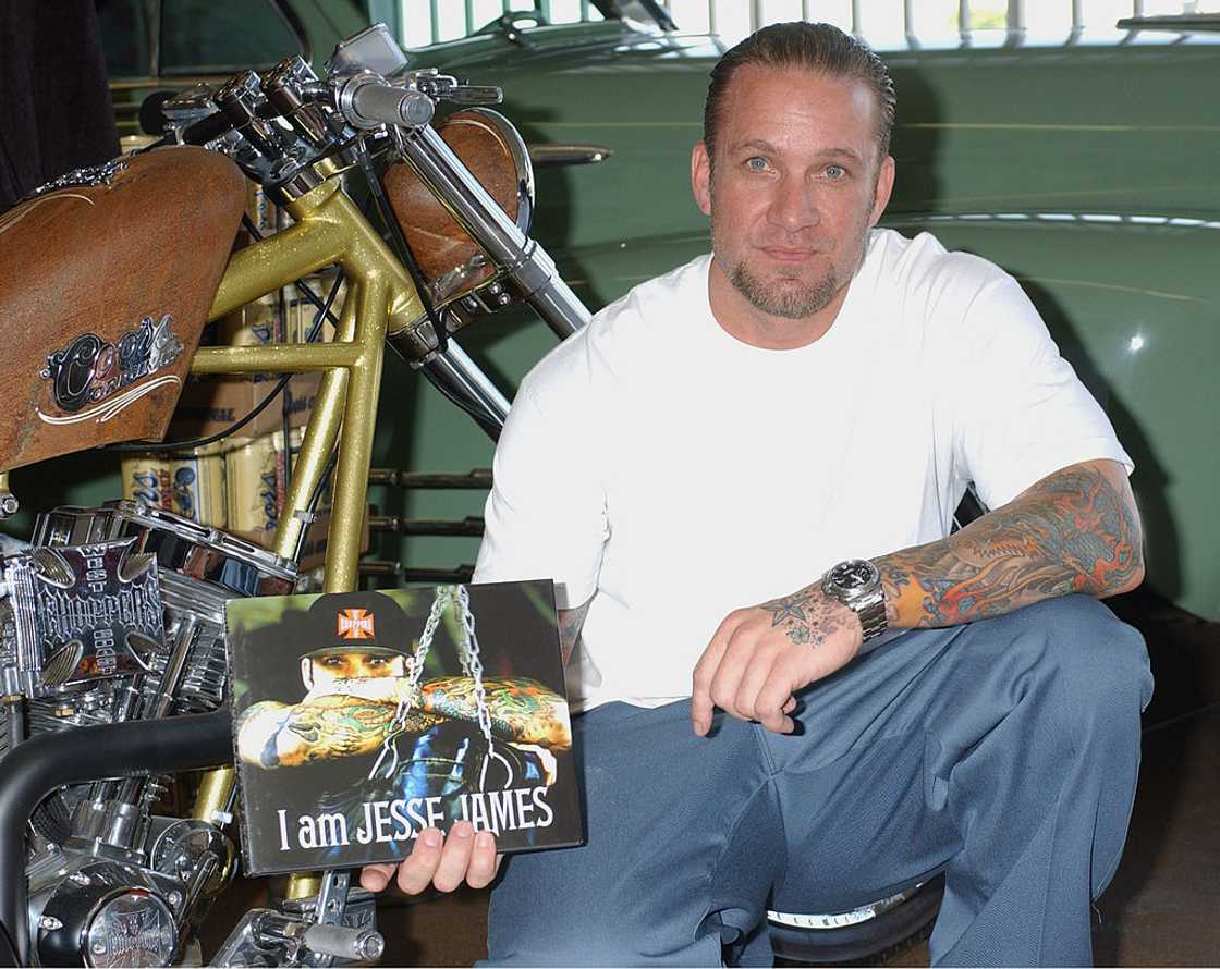 Jesse James in a white T-shirt and jeans crouching beside a gold custom chopper and holding his book "I Am Jesse James" Jesse James in a white T-shirt and jeans crouching beside a gold custom chopper and holding his book "I Am Jesse James"