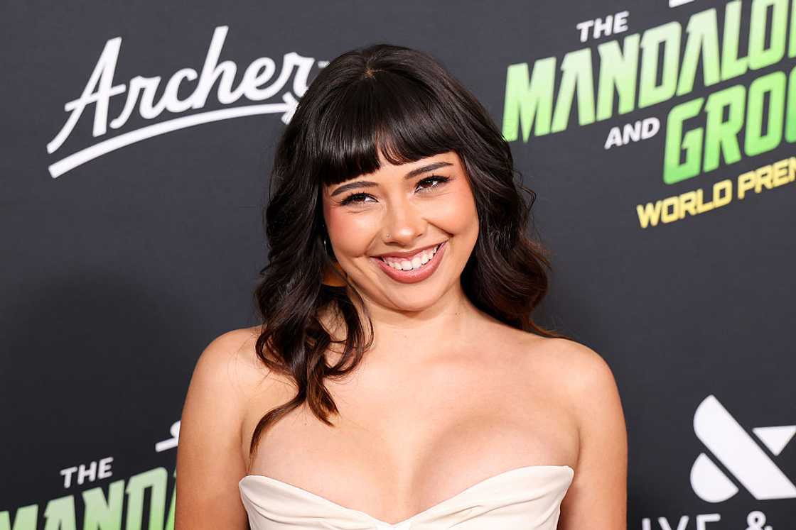 Xochitl Gomez in a strapless cream dress poses in front of a Mandalorian and Grogu premiere backdrop. Xochitl Gomez in a strapless cream dress poses in front of a Mandalorian and Grogu premiere backdrop.