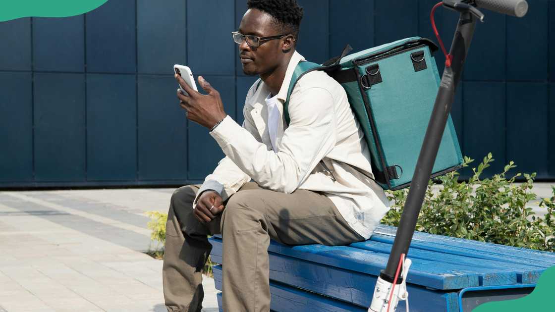 A man sits on a bench while using his phone