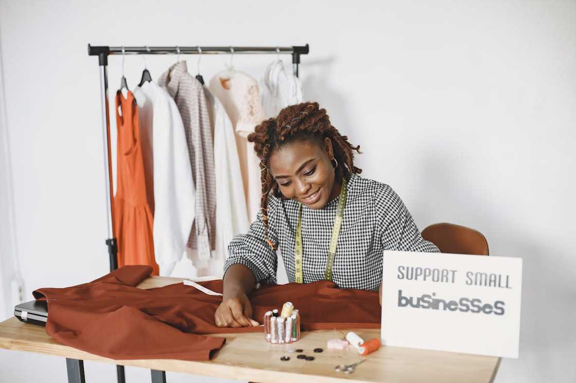 A woman sews clothing at a worktable with fabric and tools. A woman sews clothing at a worktable with fabric and tools.