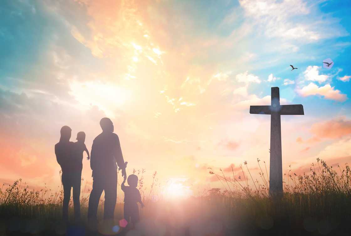 Silhouette of a father, mother and two children looking at the cross during sunset