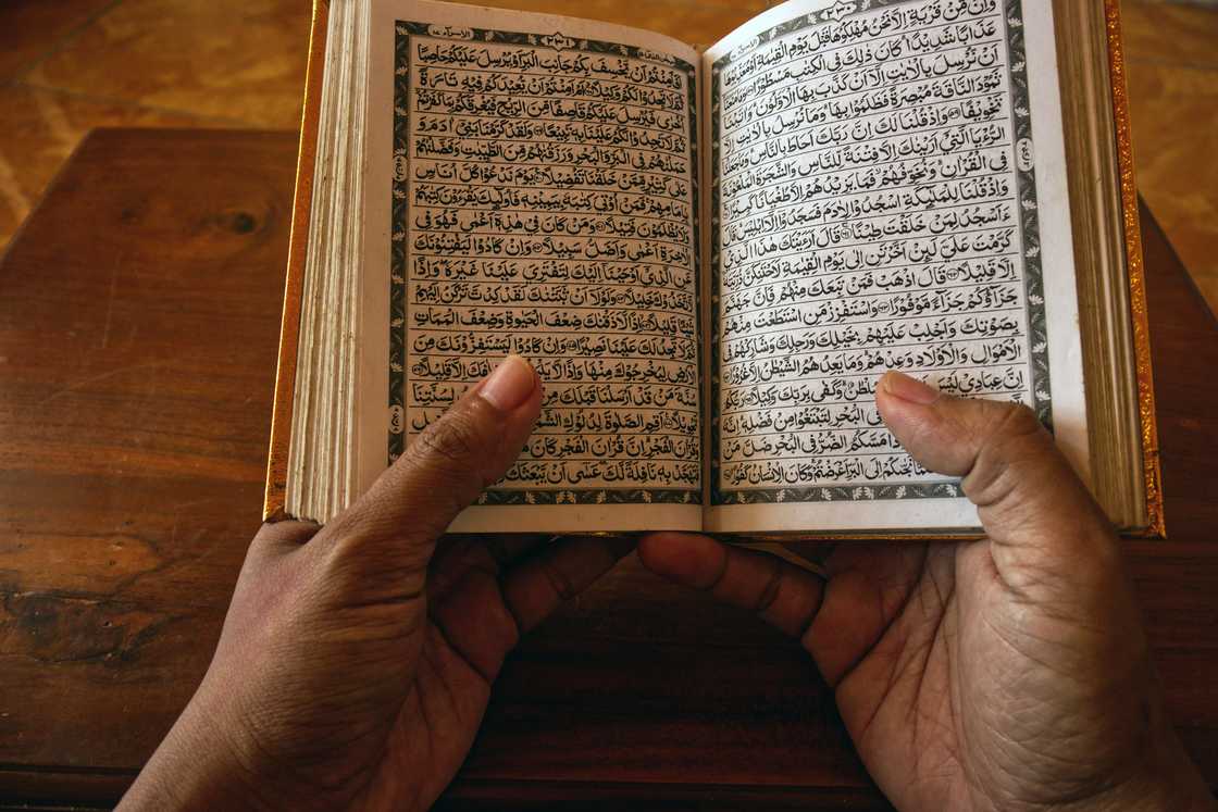 A person's hands are captured holding an open Quran